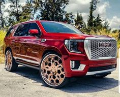 the front end of a red gmc suv parked in a parking lot with trees behind it