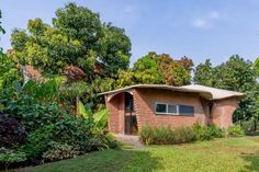 a small brick house surrounded by lush green trees and bushes on a sunny day in the jungle