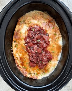 a crock pot filled with meat and cheese on top of a table next to a fork