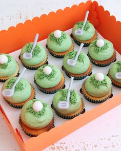 cupcakes decorated with green frosting and golf balls are in an orange box