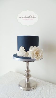 a blue and white wedding cake on a silver stand with flowers in the top tier