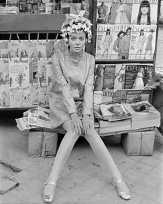 a black and white photo of a woman sitting on a bench in front of magazines