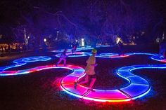 people are walking around in the dark with colorful lights on them and there is a circular pathway