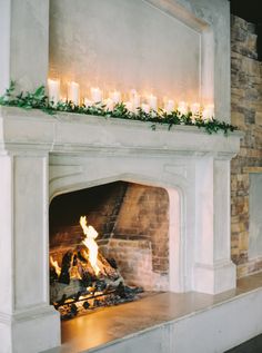 a fireplace with lit candles and greenery on the mantle