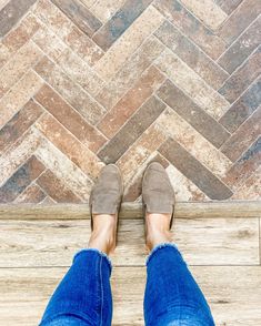 a person wearing blue jeans and brown shoes standing on a wooden floor with their feet up