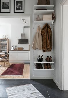 an open closet with shoes and coats hanging on the wall, next to a rug