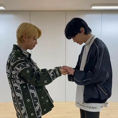 two young men standing next to each other in front of a wooden floor and wall