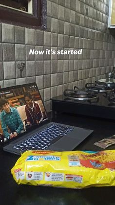 an open laptop computer sitting on top of a counter next to a bag of chips