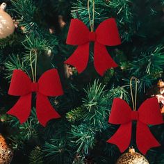 three red bows hanging from the top of a christmas tree with baubles on it