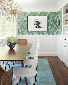 a dining room table with white chairs and a blue rug in front of the wall