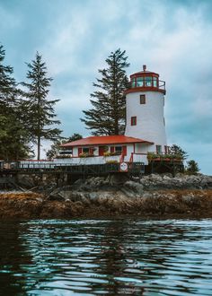 a light house sitting on top of a small island next to the ocean with pine trees around it