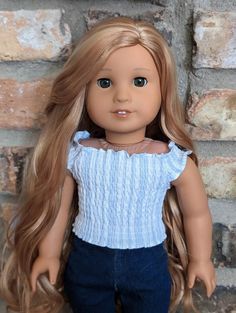 a doll with long blonde hair standing in front of a brick wall and wearing blue jeans