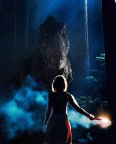 a woman standing in front of a large animal with her arm out and light coming from it's mouth