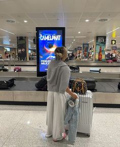 a woman standing in front of an airport baggage claim area with her suitcase and luggage