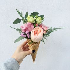 a person holding an ice cream cone with flowers in it