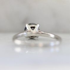 a white gold engagement ring with a black diamond in the center on a plain surface