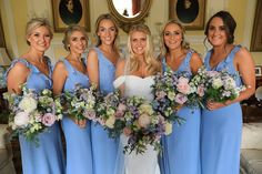 a group of women standing next to each other in blue dresses holding bouquets and smiling