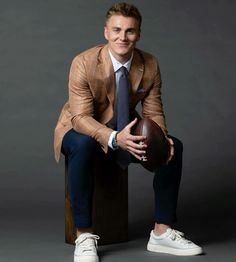 a man in a suit and tie sitting on a stool holding a football ball with both hands