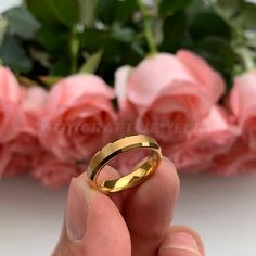 a hand holding a gold wedding ring in front of pink roses