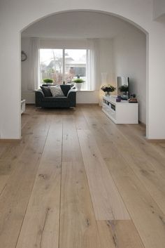 a living room with white walls and wood flooring in the center is an arch leading to a large window