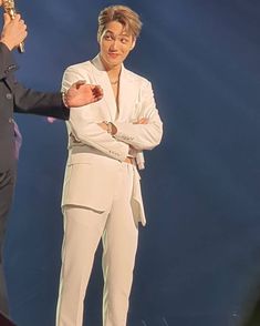 two men standing on stage one holding an award and the other wearing a white suit