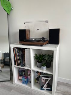 a record player sitting on top of a white book shelf next to a green plant