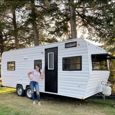 a woman standing in the doorway of a white trailer parked on top of a grass covered field