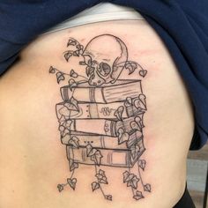 a woman's back with a skull and books tattoo on her lower arm, which is covered in ivy