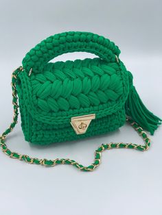 green crocheted bag with gold hardware and tassels on the handle, sitting on a white surface