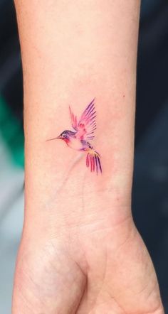 a small hummingbird tattoo on the wrist is shown in pink and purple colors,