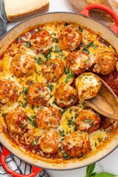 a skillet filled with meatballs and cheese on top of a white table next to bread