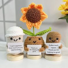 three small crocheted dolls holding signs with words written on them and a sunflower in the background