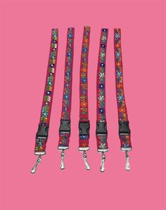 three colorful leashs on a pink background with white and black straps, one has an orange flower design