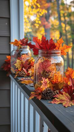 three mason jars filled with autumn leaves and pine cones sitting on a porch rail next to a window