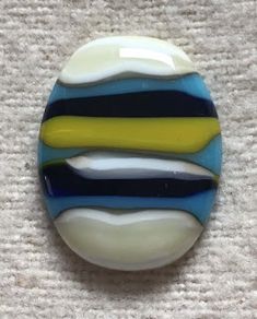 a blue, yellow and white striped glass brooch sitting on top of a carpet