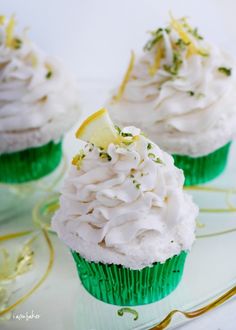 three cupcakes with white frosting and lemon wedges on a glass plate