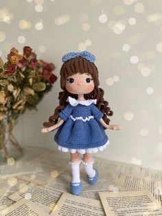 a crocheted doll standing on top of an open book with flowers in the background