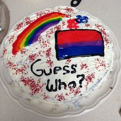 a cake with white frosting that says guess who? and a rainbow on it