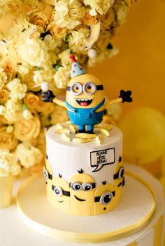 a yellow and white cake with a minion figure on top, surrounded by flowers