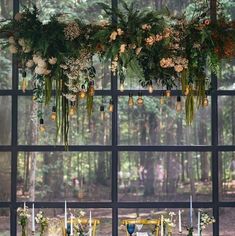 an arrangement of flowers and greenery hangs from the ceiling in front of a window