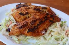 a white plate topped with chicken and coleslaw on top of a wooden table