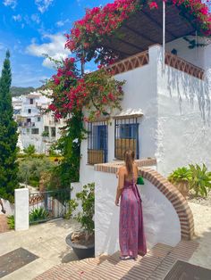 a woman in a dress is standing on the steps to a white building with pink flowers