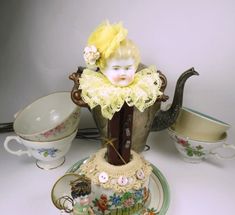 there is a tea pot with a doll in it and other items on the table