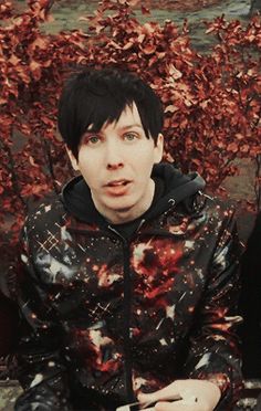 a young man sitting in front of a tree with his mouth open and tongue out