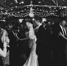 a black and white photo of a bride and groom dancing at their wedding reception with guests