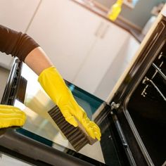 a woman in yellow gloves cleaning an oven