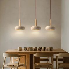 three lights hanging over a wooden table with chairs