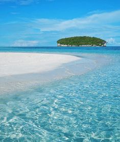 an island sits in the middle of clear blue ocean water, with white sand and green trees