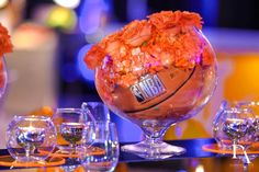 an arrangement of flowers and wine glasses on a table with basketballs in the center