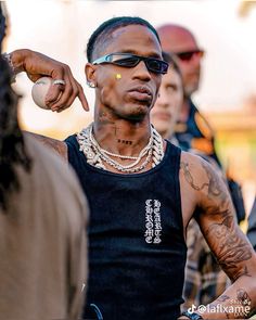 a man with tattoos holding a baseball in one hand and pointing to the ball in the other